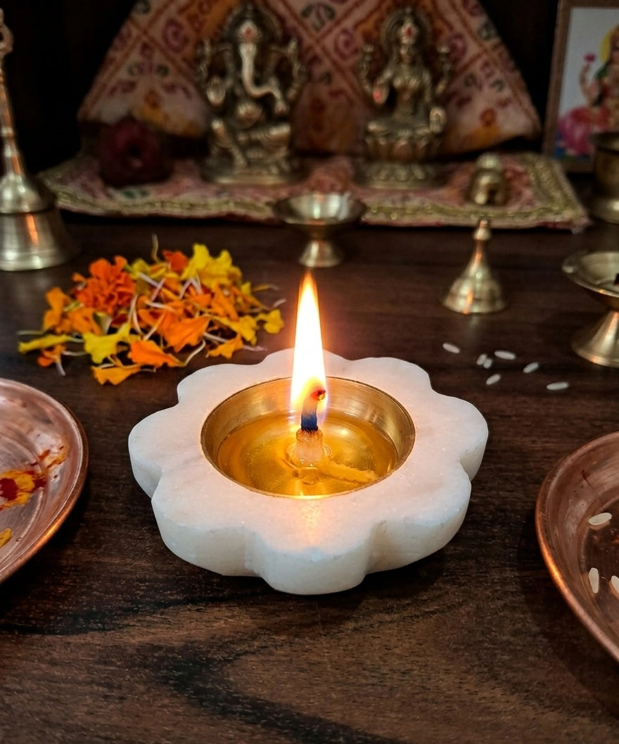 lotus flower shaped marble diya filled with oil and burning flame on wooden altar