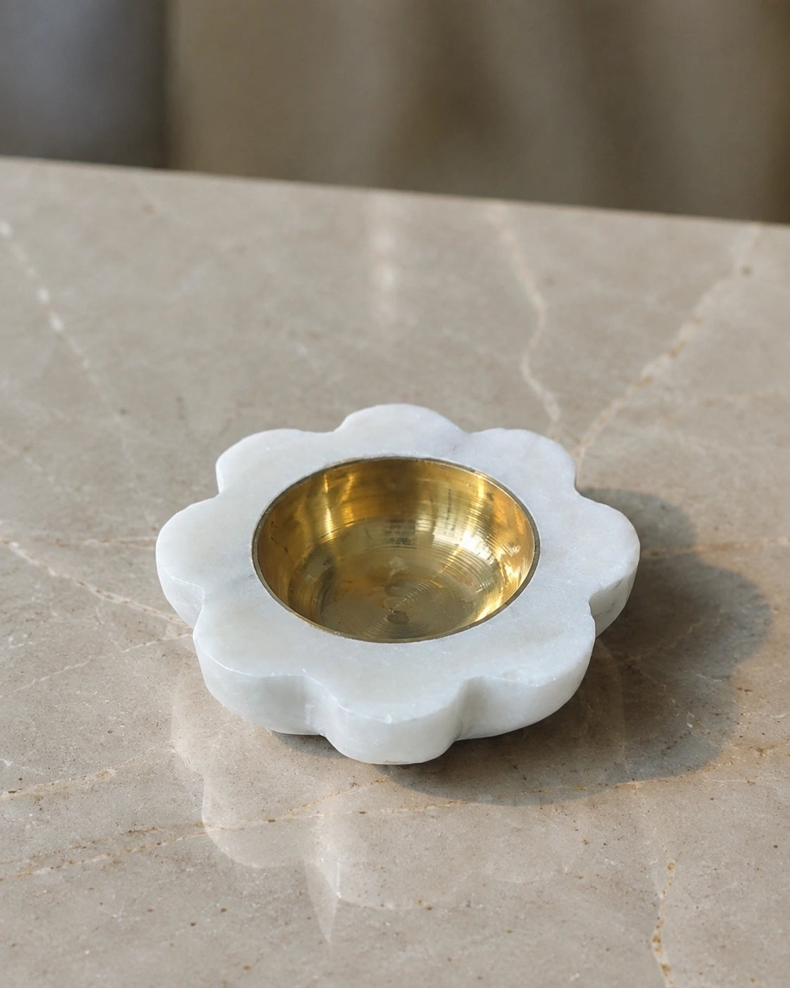 handcarved white marble petal diya with brass cup holding lit wick in home mandir