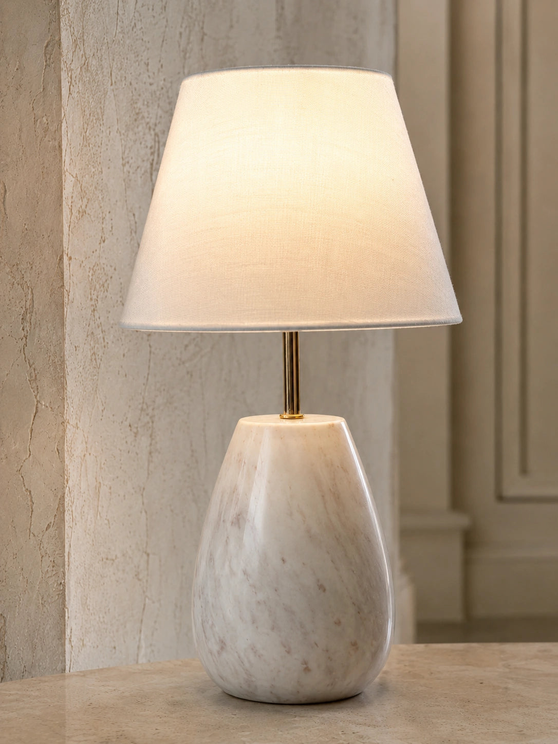 Close-up of white stone-look table lamp with gold-tone detailing and textured shade